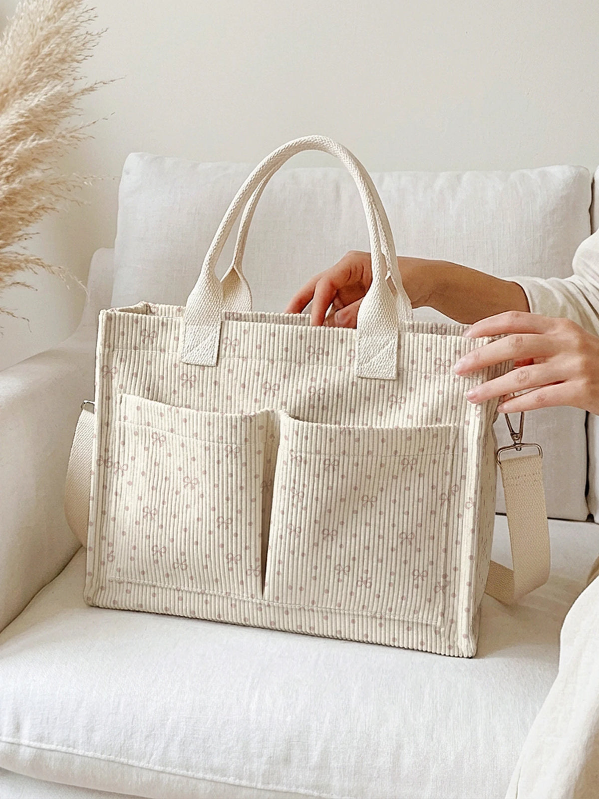 Un sac cabas beige en velours côtelé avec une poignée et deux poches repose sur un canapé blanc.