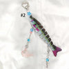 A silver acrylic keychain charm shaped like a fish with colorful accents and a heart loop.