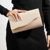 A woman holds a light beige velvet evening clutch with a gold accent against a black ribbed dress.