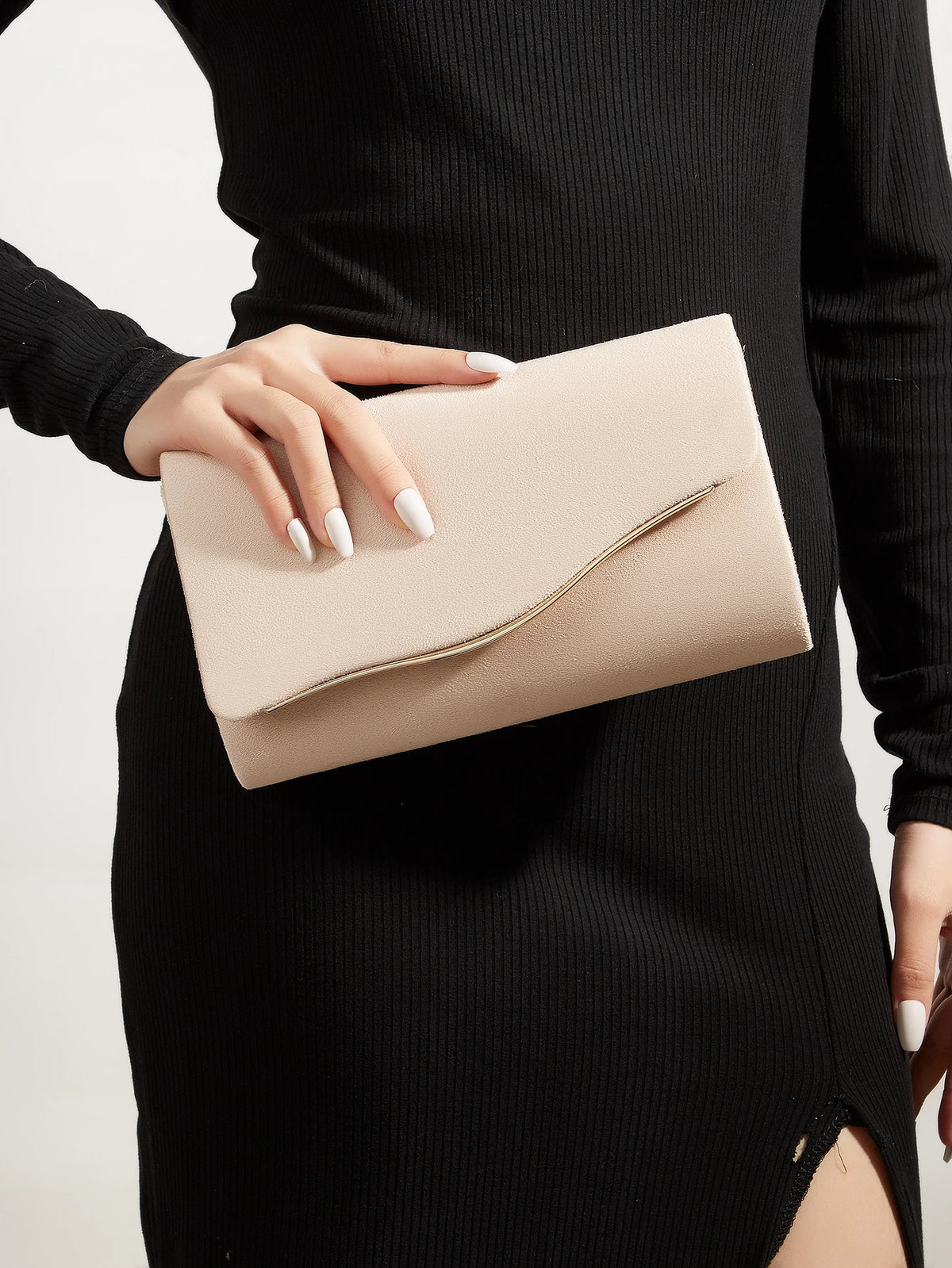 A woman holds a light beige velvet evening clutch with a gold accent against a black ribbed dress.