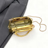 A small gold metal clutch bag with a gold chain strap is shown against a gray fabric background.