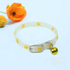 A clear pet collar with yellow paw prints and a gold-colored tag, next to an orange flower.