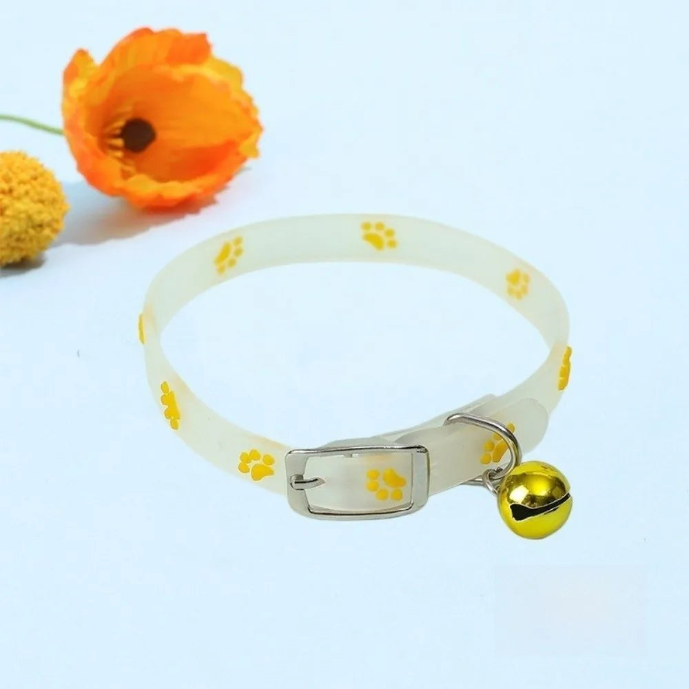 A clear pet collar with yellow paw prints and a gold-colored tag, next to an orange flower.