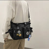 A person wearing a cream hoodie holds a black nylon crossbody bag with various charms.