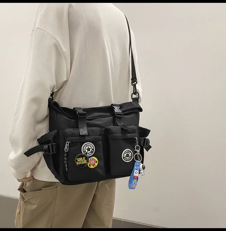 A person wearing a cream hoodie holds a black nylon crossbody bag with various charms.