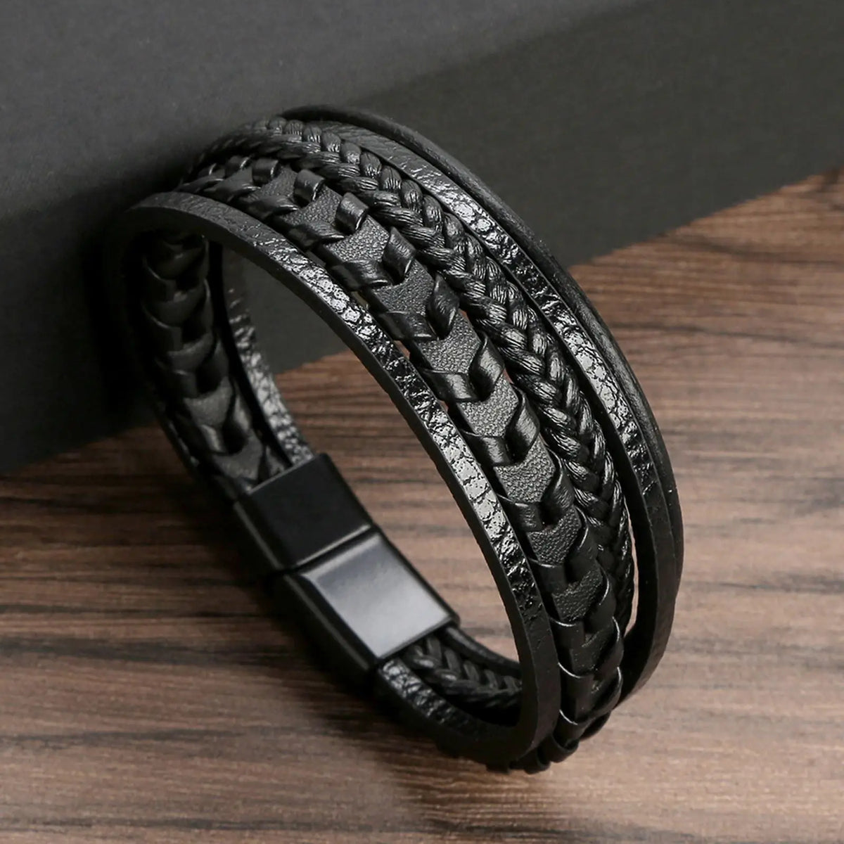 A black multi-layer leather bracelet with textured beads is shown on a wooden surface.