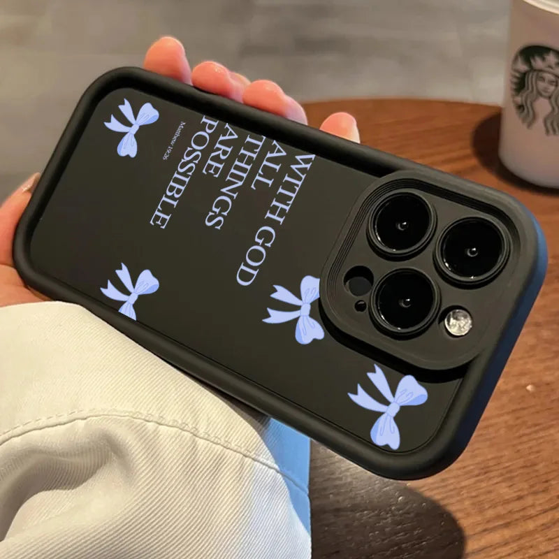 A hand holds a black silicone phone case featuring white butterfly bow graphics and the text All Things Are Possible with God