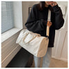 A woman holds a cream-colored crocodile grain PU leather travel duffle bag with a beige strap in a bright room.