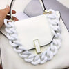 A white acrylic chunky chain shoulder strap is draped over a white handbag.