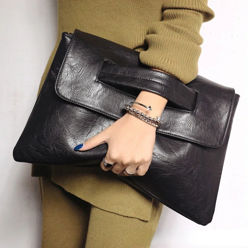 A hand holding a black leather sequined crossbody clutch bag against a beige sweater.