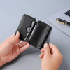 A hand holds a black magnetic foldable ID card holder and coin purse next to a silver pen on a laptop.