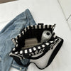Un sac bandoulière à motif rayé noir et blanc à côté d'un jean bleu.
