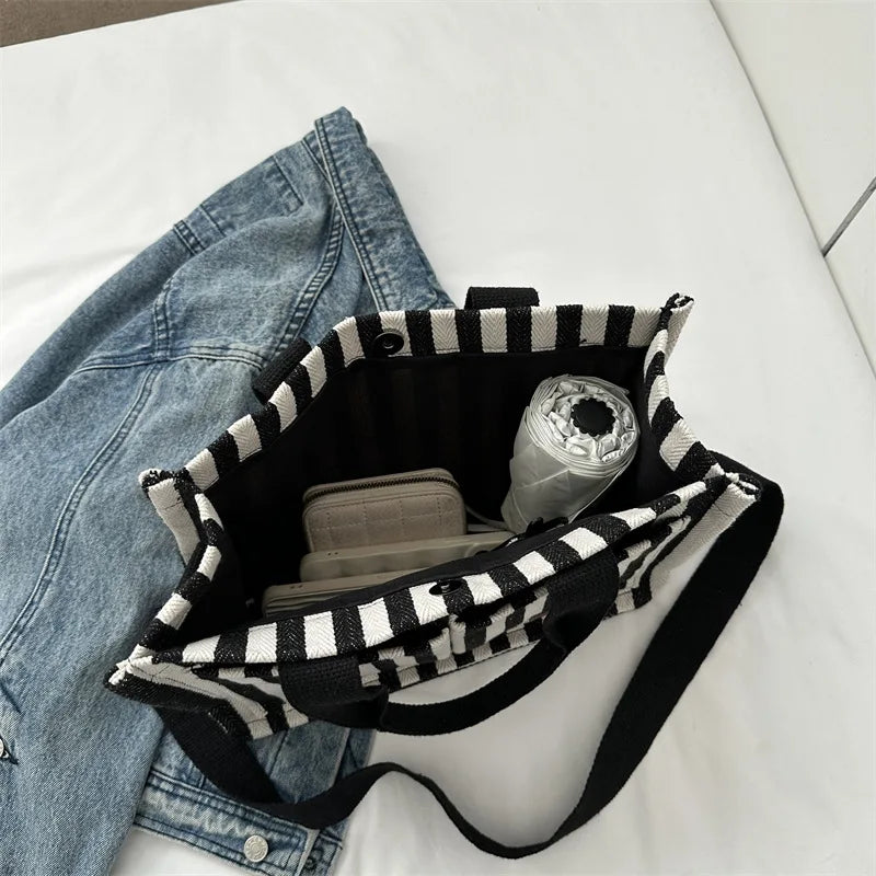 Un sac bandoulière à motif rayé noir et blanc à côté d'un jean bleu.