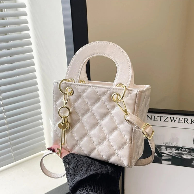 A light pink quilted leather crossbody handbag with gold chain accents resting on a white surface.
