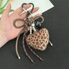 A leopard print faux fur charm keychain with brown leather straps and pearl beads is held in a hand.