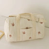 A beige quilted diaper bag tote with small pink animal embroidery sits on a white surface.