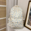 Mochila de color crema con estampado floral azul claro y múltiples bolsillos, mostrada sobre una superficie blanca.