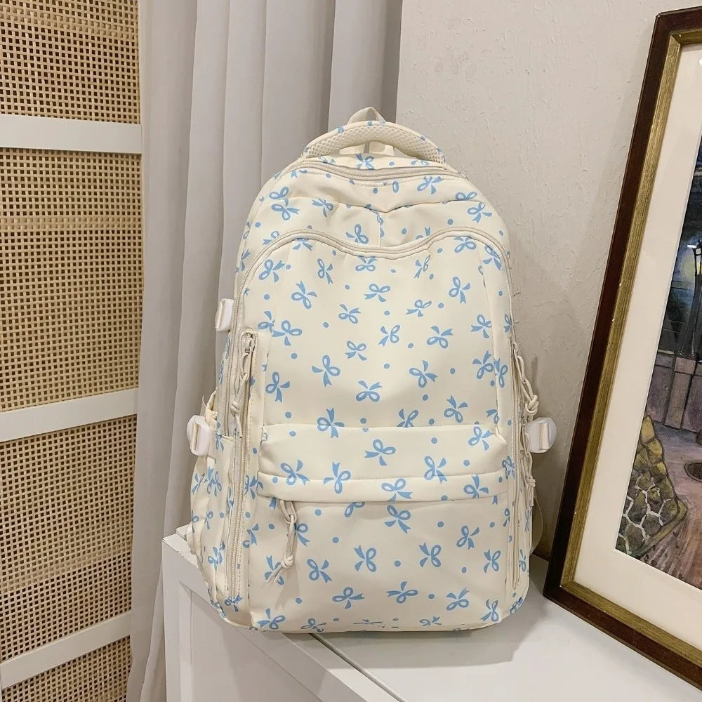 Mochila de color crema con estampado floral azul claro y múltiples bolsillos, mostrada sobre una superficie blanca.