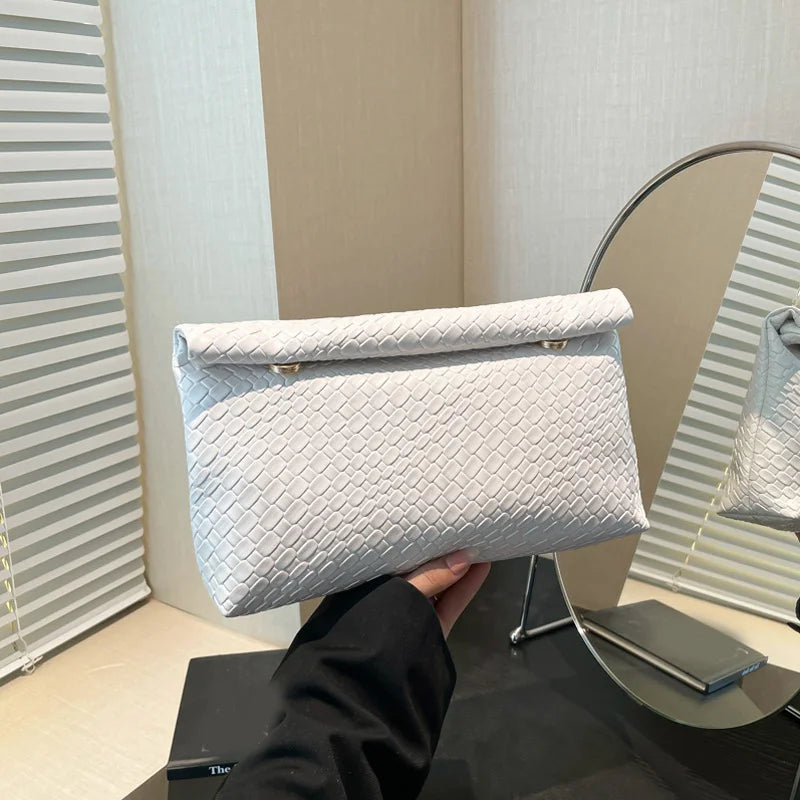 Una mano sostiene un bolso de mano tejido gris claro contra un fondo desenfocado.