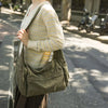 A person wearing a cream and yellow patterned sweater carries a large olive green cotton canvas shoulder crossbody bag on a s