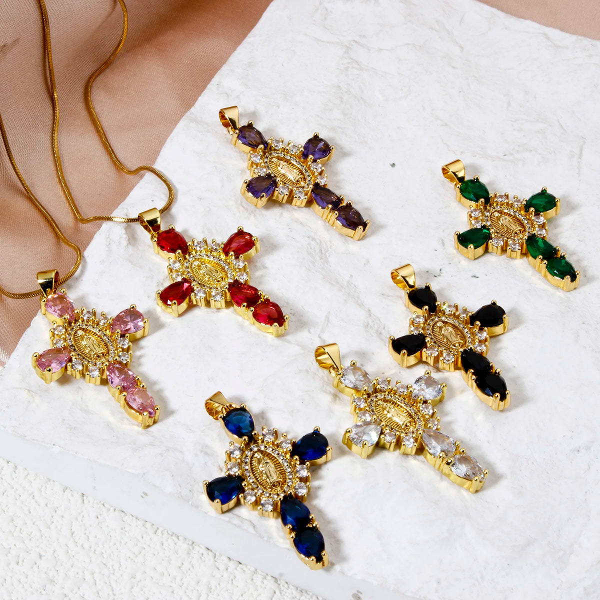 A collection of gold-plated cross and Virgin Mary charm pendants featuring various colored gemstones like ruby, emerald, and 