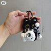 Colgante de gato peluche con rayas blancas y negras en una mano contra un fondo gris.