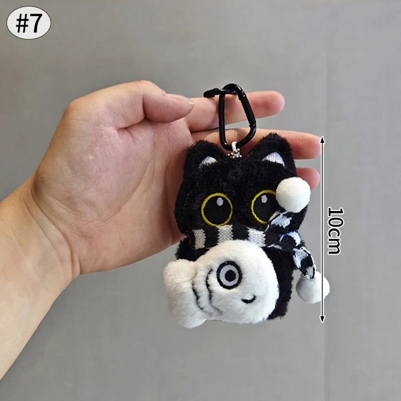 Colgante de gato peluche con rayas blancas y negras en una mano contra un fondo gris.