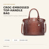 Braune krokodillede Top-Handle-Tasche mit poliertem Silhouetten-Look vor hellem Hintergrund.