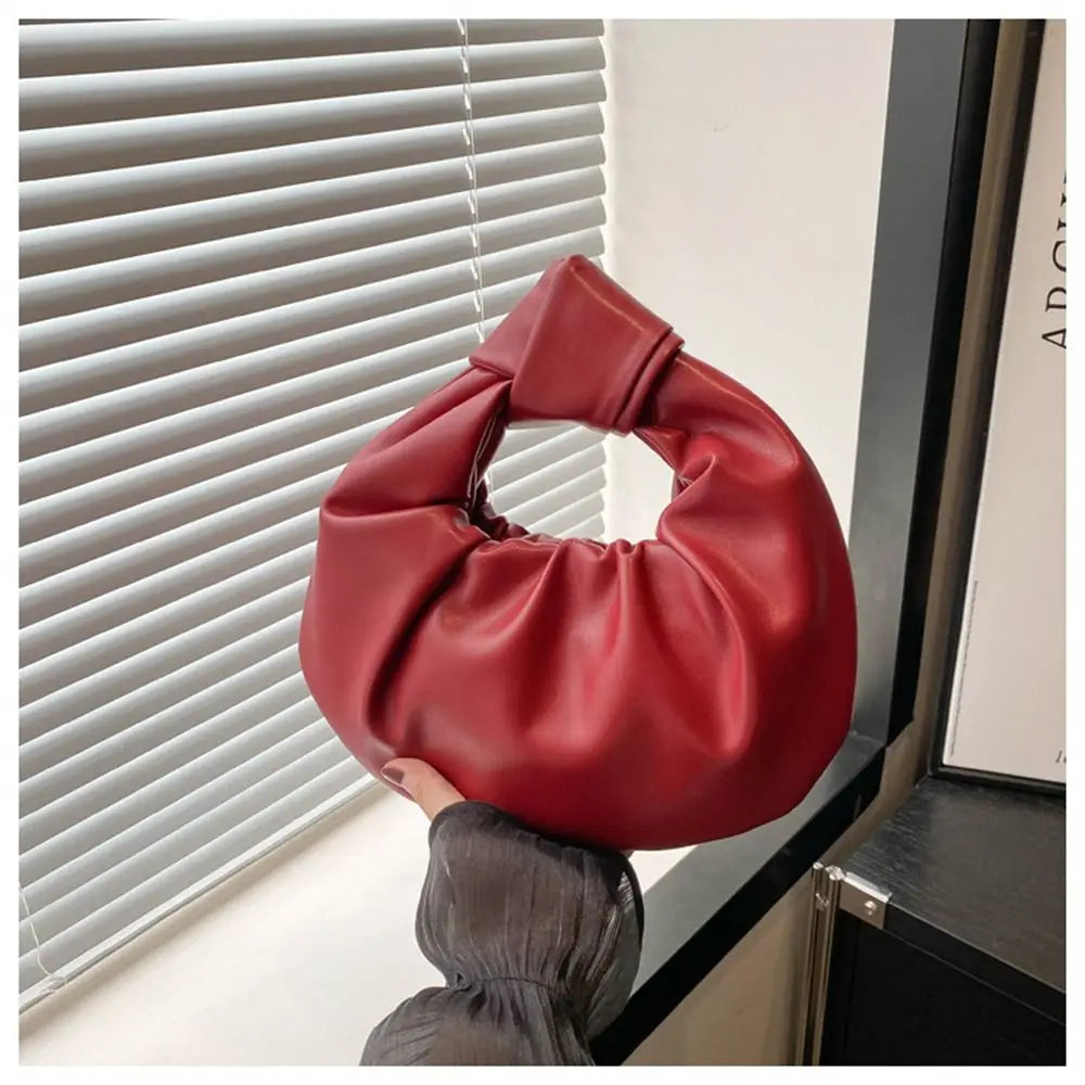 Clutch de noche con lazo de cuero rojo intenso contra una persiana.