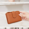 A close-up of a brown PU leather bifold wallet with a zipper closure and VIP branding being held by a hand.