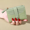 A hand holds a light green PU leather card wallet with a double zip closure.