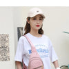 Eine Frau präsentiert eine rosa wasserdichte Crossbody-Tasche und eine beige Mütze vor hellem Hintergrund.