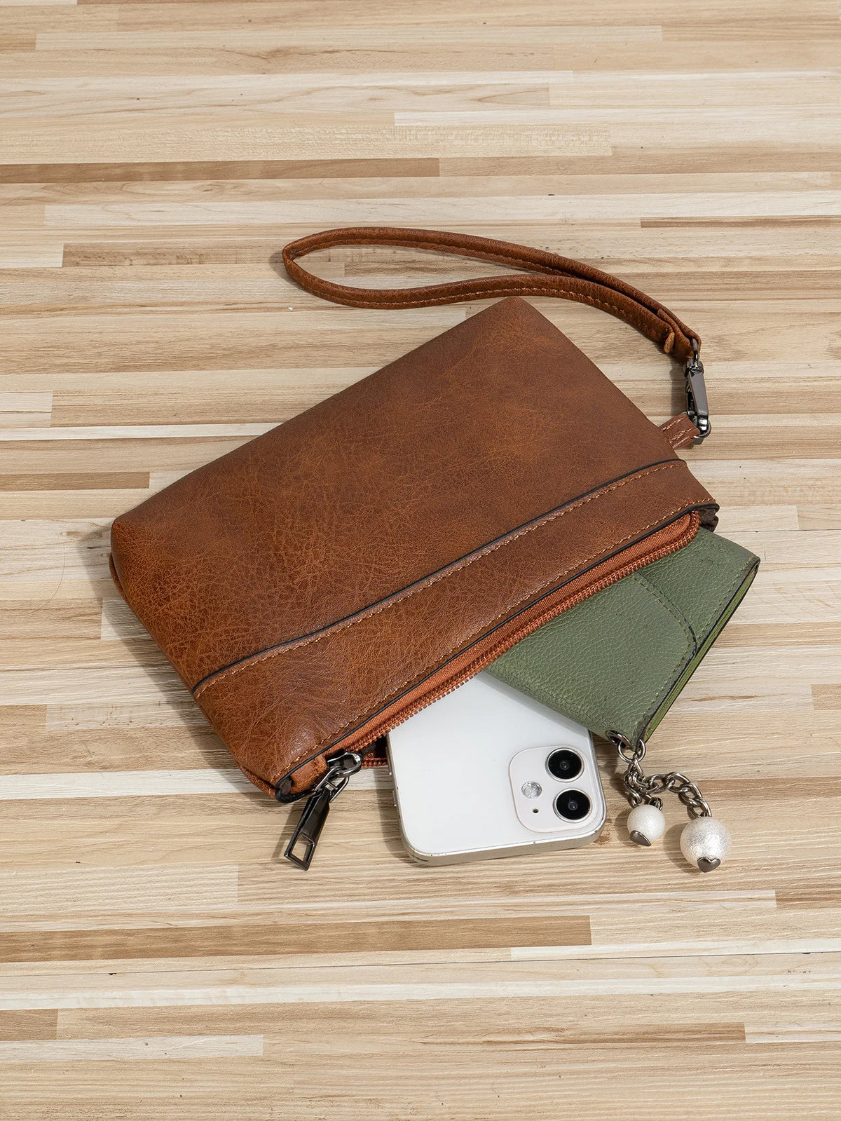 A brown retro PU leather zipper wrist bag rests on a light wooden surface next to a white smartphone.