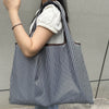 A person is holding a black and white striped foldable oxford grocery tote bag with a white sweater.