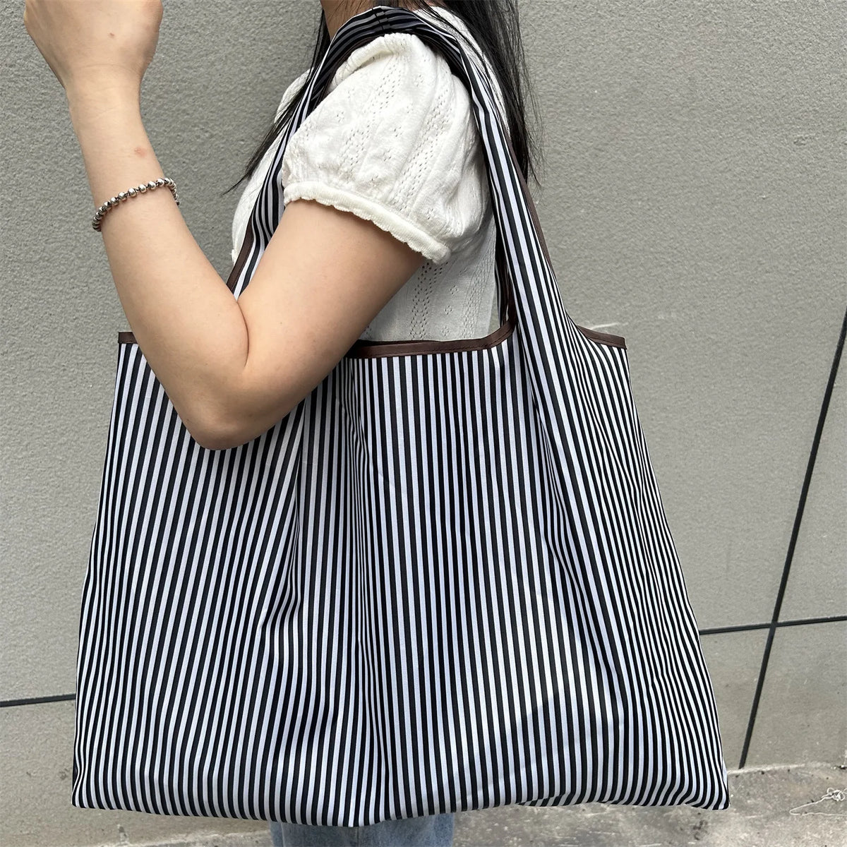 A person is holding a black and white striped foldable oxford grocery tote bag with a white sweater.