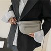 A woman holds a gray PU leather multi-pocket crossbody bag against a black blazer with striped shirt sleeves.