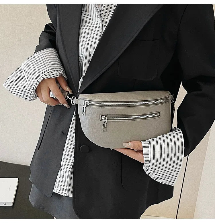 A woman holds a gray PU leather multi-pocket crossbody bag against a black blazer with striped shirt sleeves.