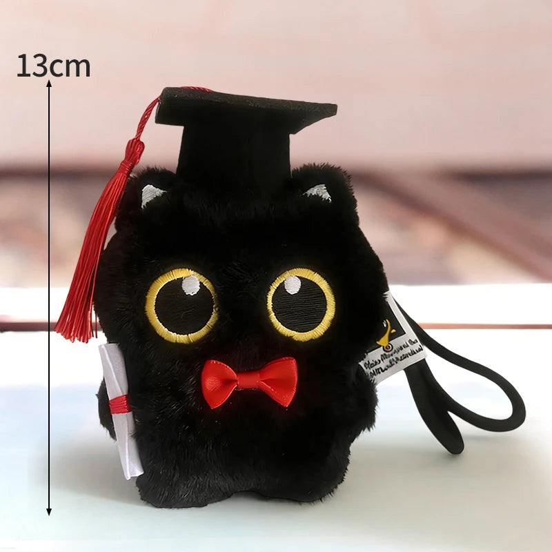 Colgante de llavero de gato negro de peluche con birrete de graduación y lazo rojo, sobre fondo blanco.