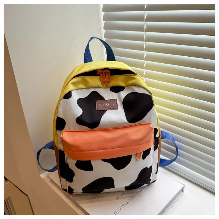 A yellow and black cow print fashion backpack with an orange pocket resting on a white surface.
