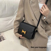 Beige Trenchcoat hält eine schwarze Lederhandtasche mit goldenen Verzierungen.
