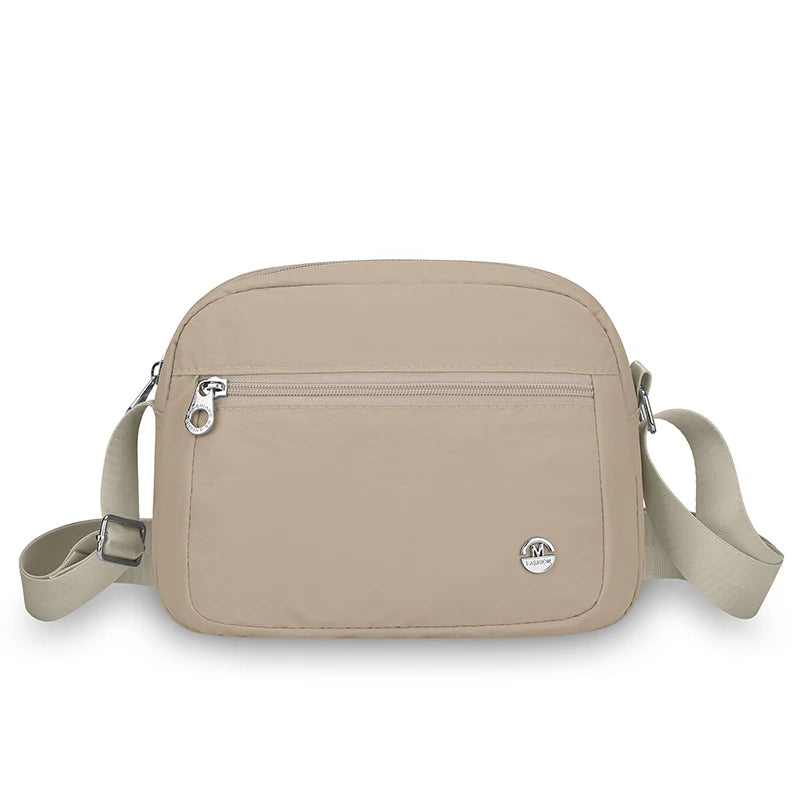 Beige Nylon-Crossbodytasche mit Klappe und verstellbarem Riemchen vor weißem Hintergrund.