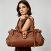 A woman holds a brown vegan leather tote bag with a gold lock buckle clip against a light gray background.