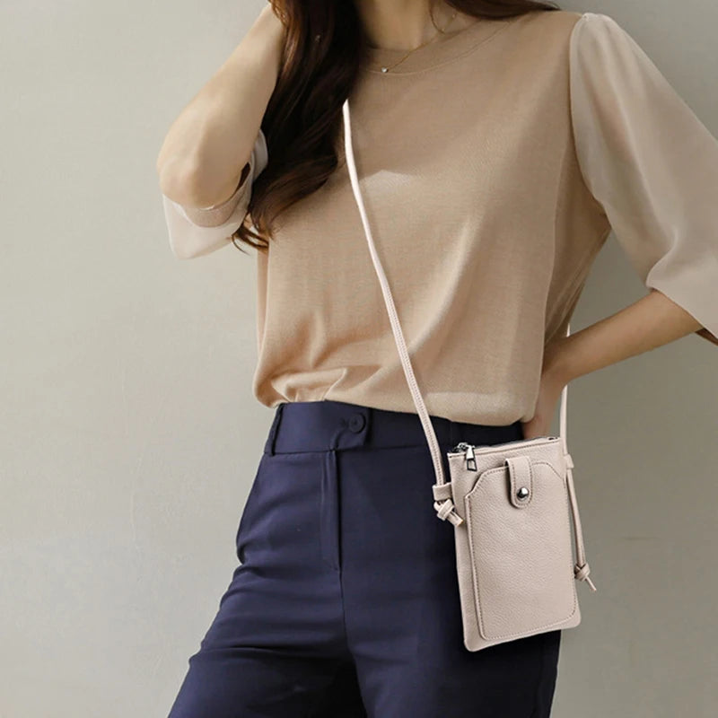 A woman wearing a beige top and dark blue pants holding a light pink compact PU leather crossbody bag.