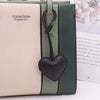A light beige leather notebook or folder with a dark green cover and a black heart keychain charm.