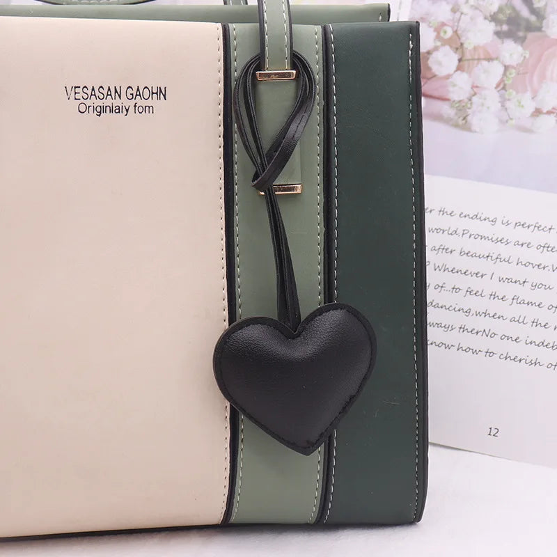 A light beige leather notebook or folder with a dark green cover and a black heart keychain charm.