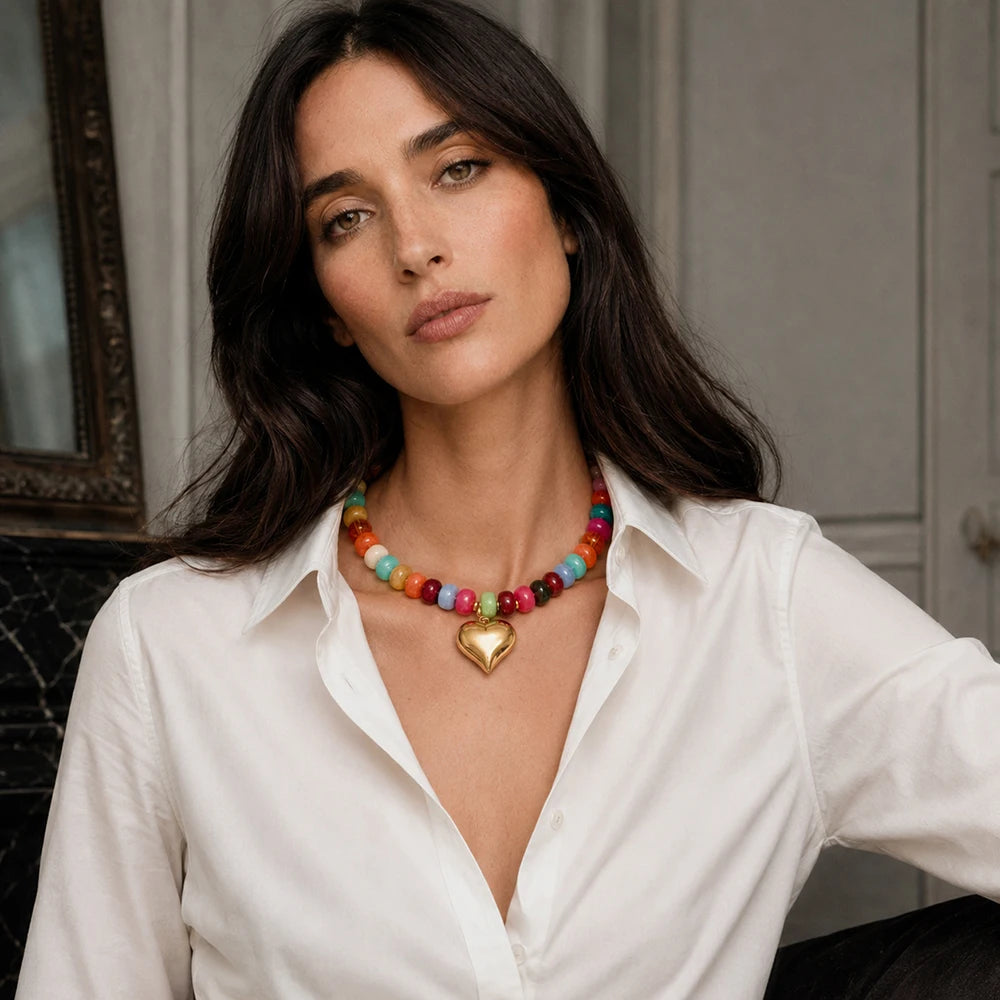 A woman wearing a colorful heart charm bead necklace with resin accents and a white collared shirt.