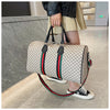 A woman holds a beige plaid travel duffle bag with black and green accents in a modern indoor setting.