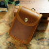 A brown leather multi-functional waist bag with a brass stud, resting on an old map.