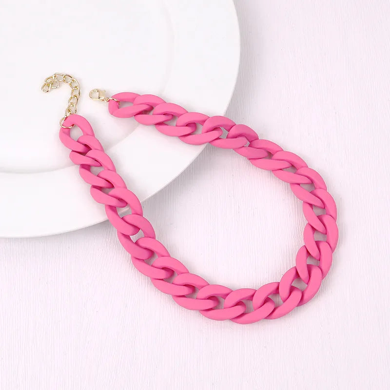 A pink acrylic statement choker necklace with a gold-colored clasp is displayed on a white background.