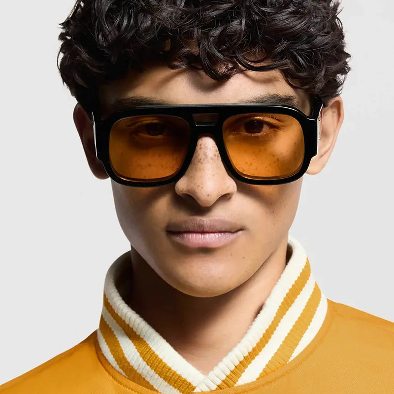 A male model wearing vintage leopard print oversized square sunglasses and a yellow sweater.